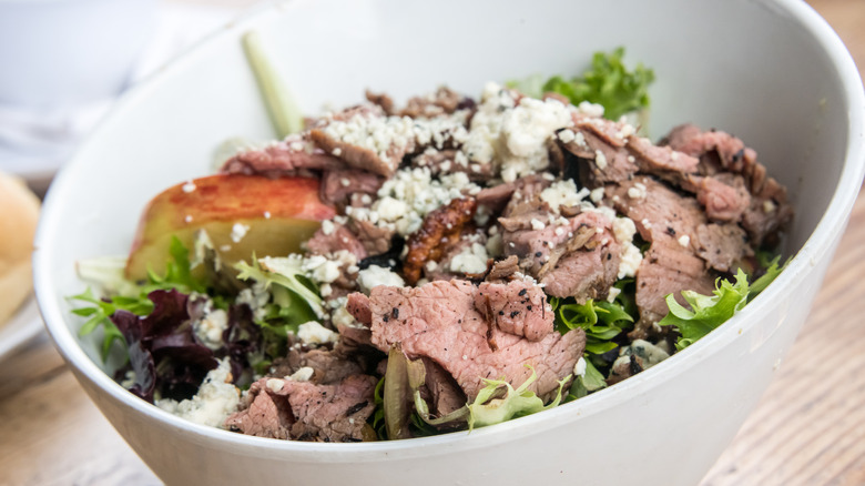 Blue cheese mixed into a steak salad with lettuce, mixed greens, and apple.
