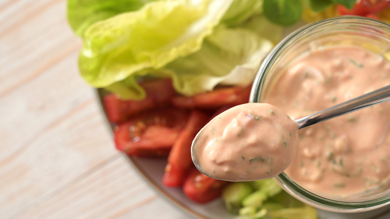 A spoon lifting Thousand Island dressing from a bowl