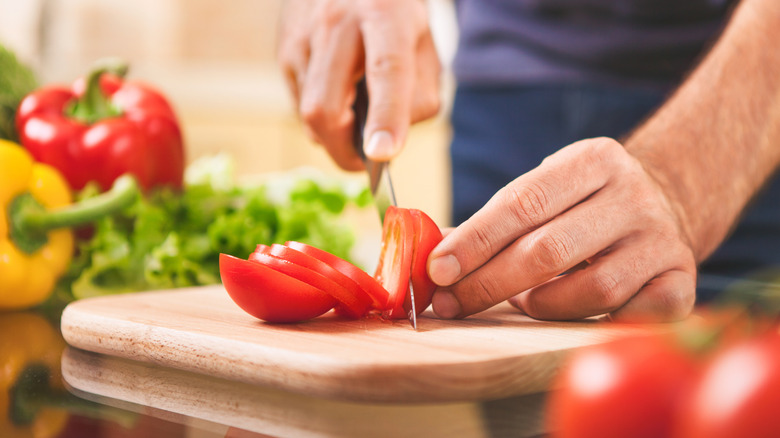 A person's hands are seen slicing tomatoes on a cutting board.