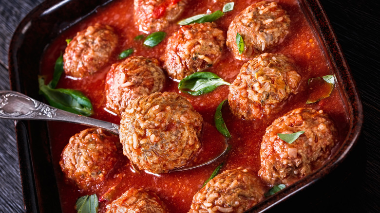 A pan of porcupine meatballs in tomato sauce with fresh basil.