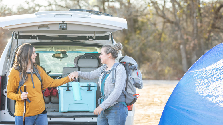 two women unloading a blue cooler at a campsite