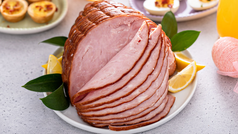 Sliced ham on a plate surrounded by other accoutrements. .