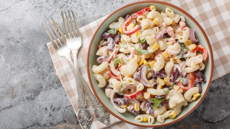 A bowl of traditional Mexican macaroni salad with onions, bell peppers, corn, and mayonnaise with two forks alongside.
