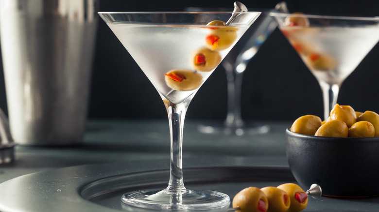 Shaken dry martinis served with pimento-stuffed olives next to a bowl of olives