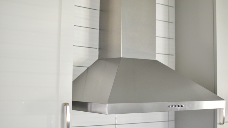 A steel range hood between two kitchen cabinets.