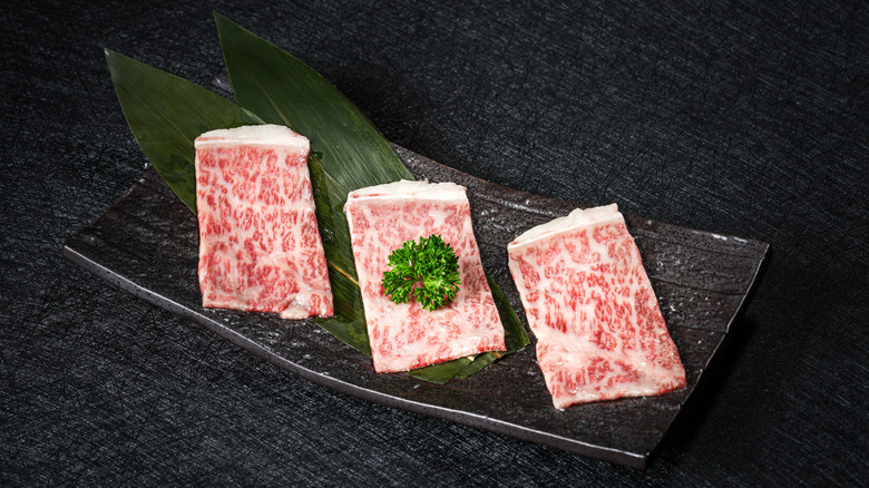 Raw pieces of premium wagyu with heavy marbling on a black plate
