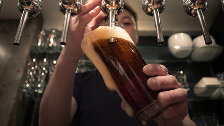 A bartender pours a glass of foamy beer from a metal tap
