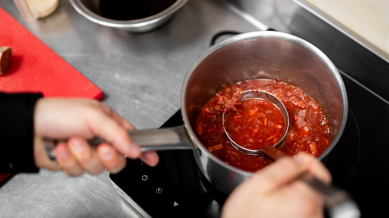 chef in kitchen stirring tomato sauce in a silver pan