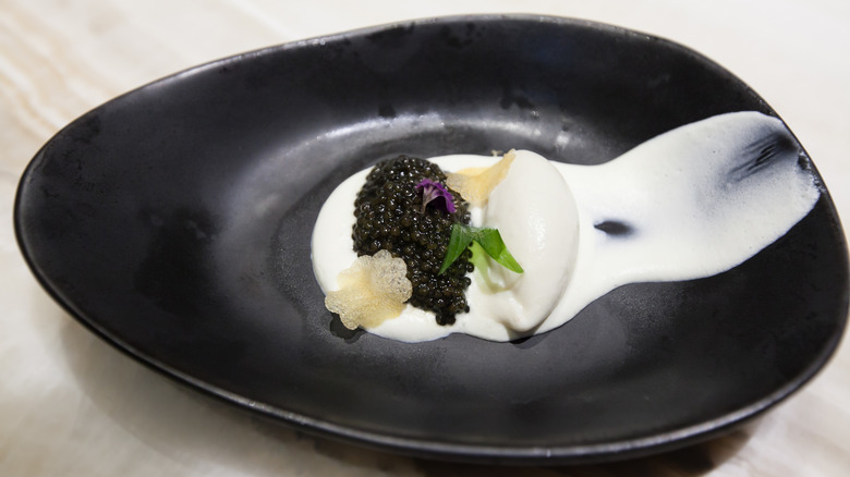 Quenelles of black caviar and white ice cream on a black oval plate with garnishes