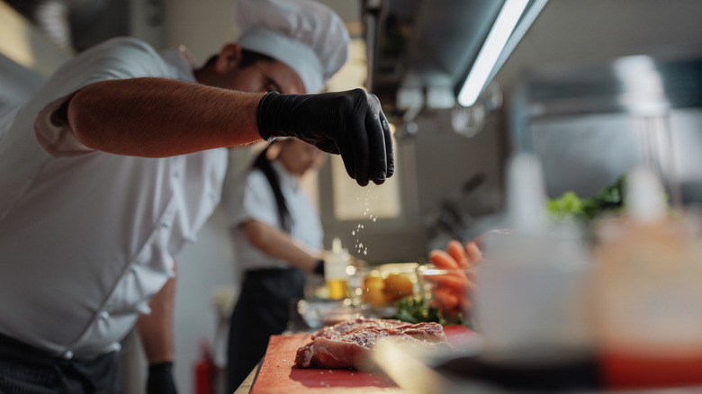 A chef's hand is seen salting food from several inches in the air.