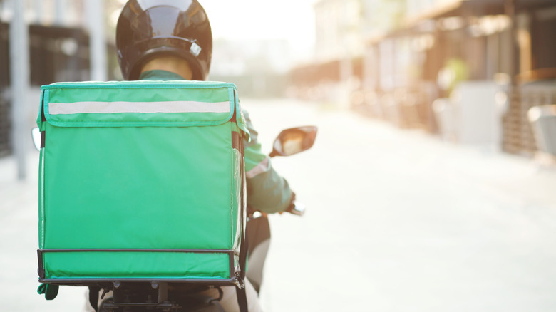 Delivery driver on a moped with a green food carrier