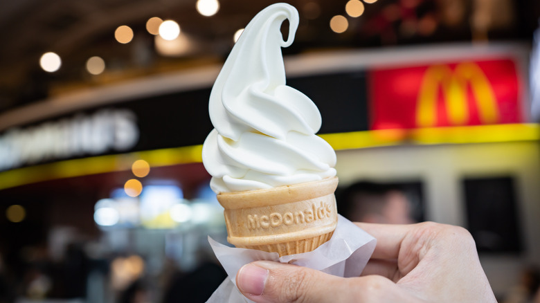 A hand holding a vanilla ice cream cone from McDonald's
