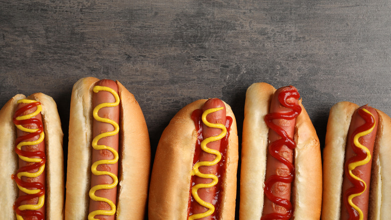 Hot dogs in buns with ketchup and mustard lined up on a grey background