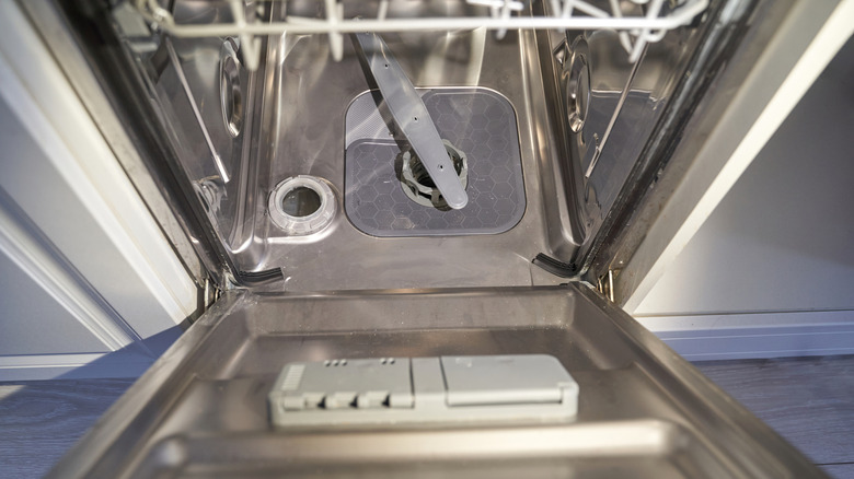 An open dishwasher showing the spray arm and detergent compartment
