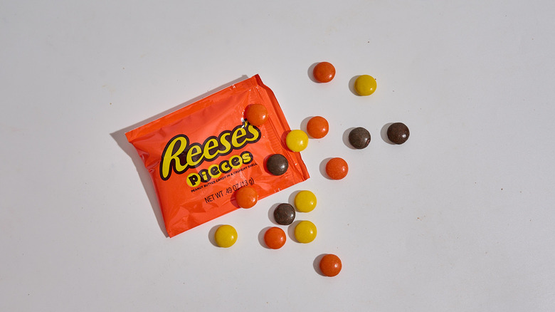 Package of Reese's Pieces on a table with a handful of Reese's Pieces