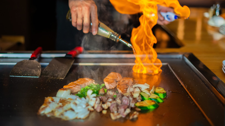 A teppanyaki chef adding oil to salmon and vegetables on a flat iron griddle