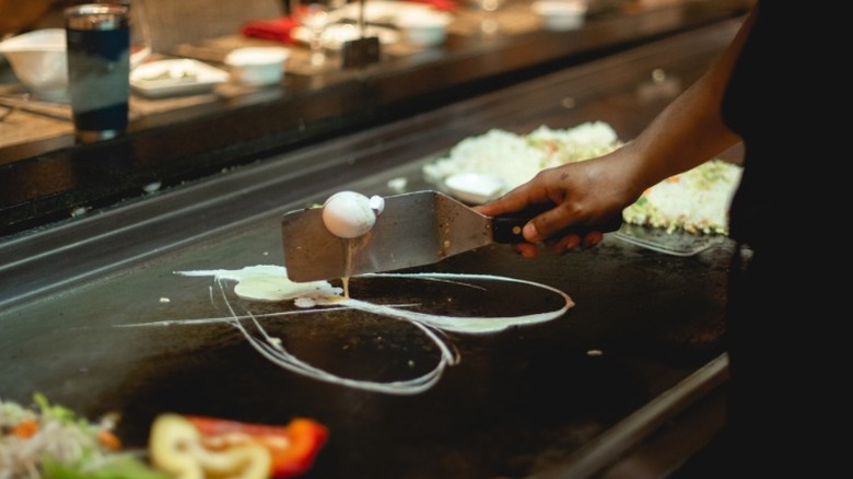 A chef cooking eggs on a teppanyaki grill for customers