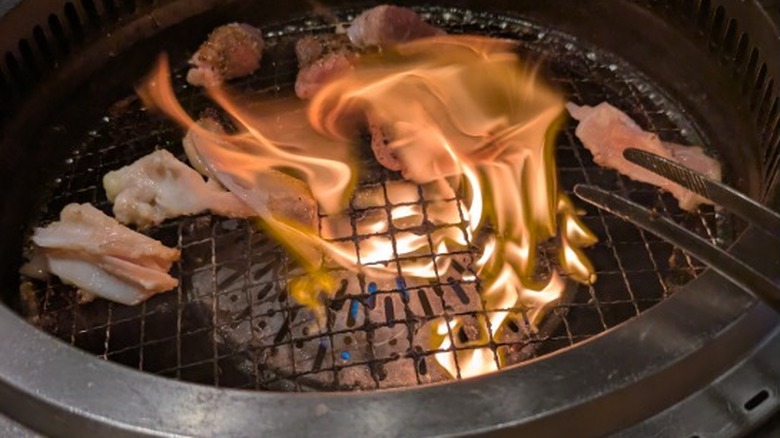 Meats being cooked over an open flame on a hibachi style grill