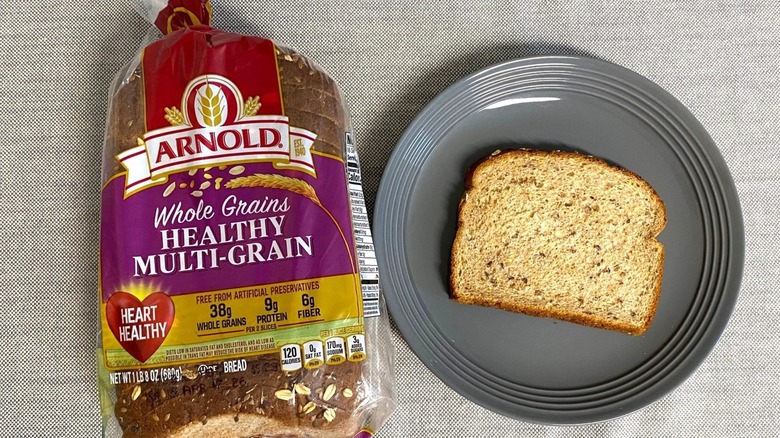 Bag of Arnold Whole Grains Healthy Multi-Grain Bread beside a slice on gray plate