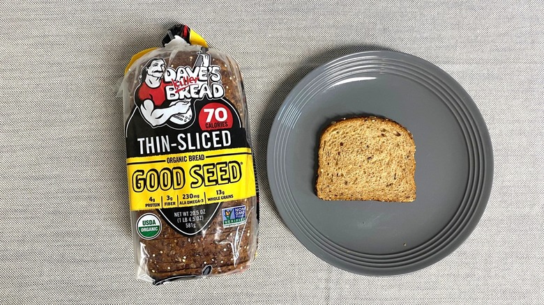 Bag of Dave's Killer Bread Thin-Sliced Good Seed beside a slice on gray plate
