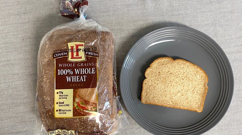 Bag of L'Oven Fresh Whole Grains 100% Whole Wheat Bread beside a slice on gray plate