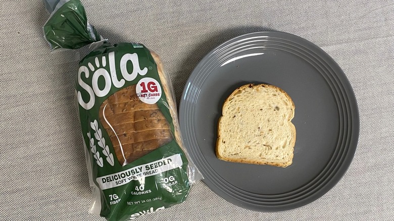 Bag of Sola Deliciously Seeded Soft White Bread beside a slice on gray plate