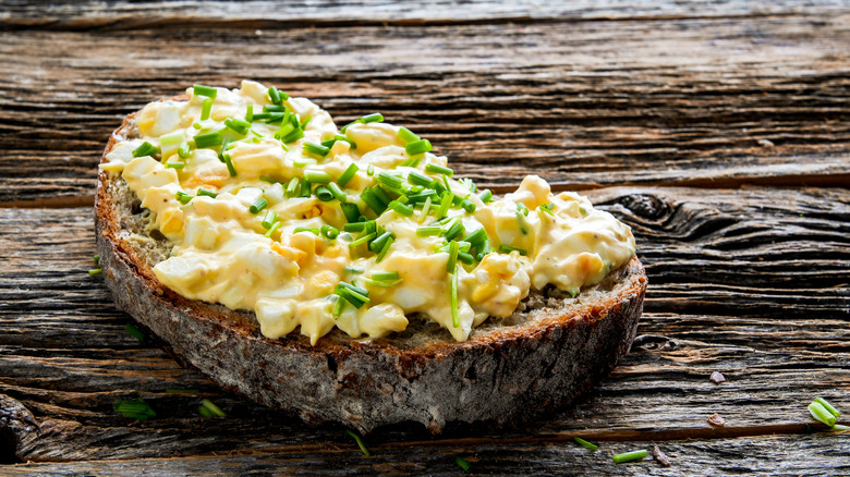 A piece of bread with egg salad on a wooden table.