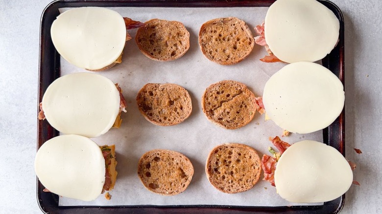 English muffin halves on parchment-lined baking sheet topped with prosciutto and provolone