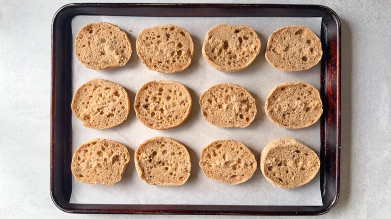 English muffin halves arranged on a parchment-lined baking sheet