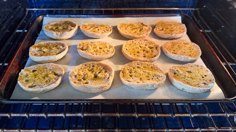 English muffin halves on parchment-lined baking sheet in oven