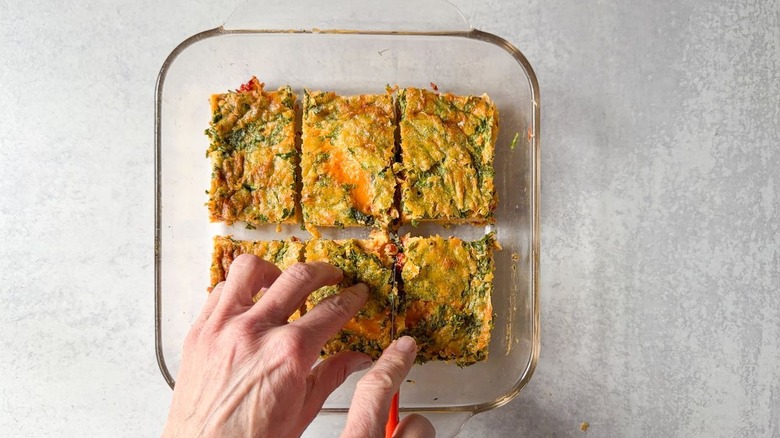 Cutting baked eggs into rectangles with small knife in square glass baking dish