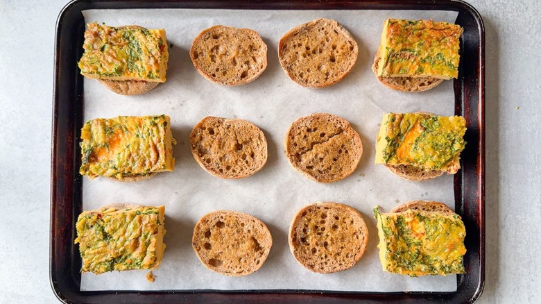 English muffin halves with baked egg rectangles on parchment-lined baking sheet