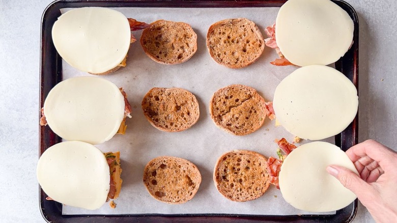 Placing provolone slices on high-protein English muffin sandwiches