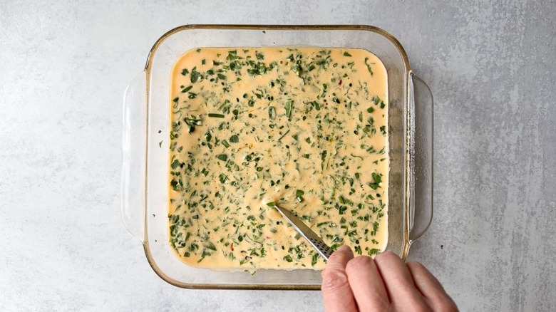 Mixing vegetables into egg filling mixture in glass baking dish with tip of a knife