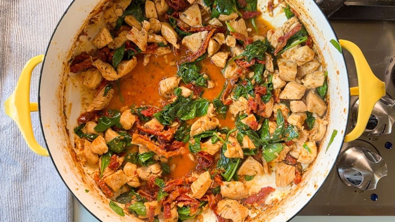 Chicken, sundried tomatoes, spinach and sauce in yellow pot on stovetop