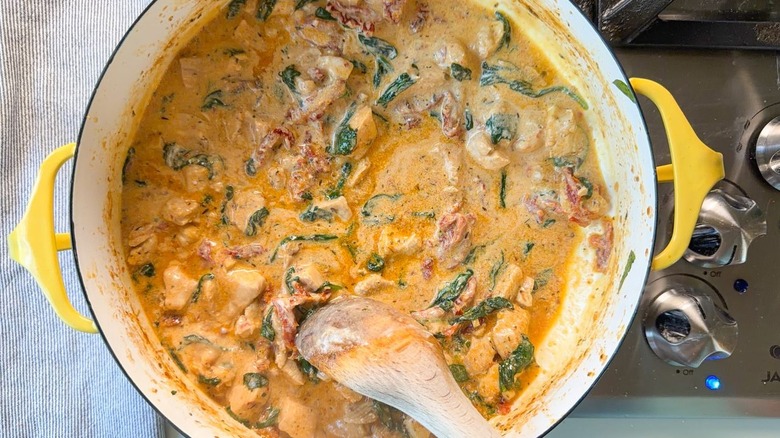 Stirring marry me chicken in yellow pot on stovetop with wooden spoon