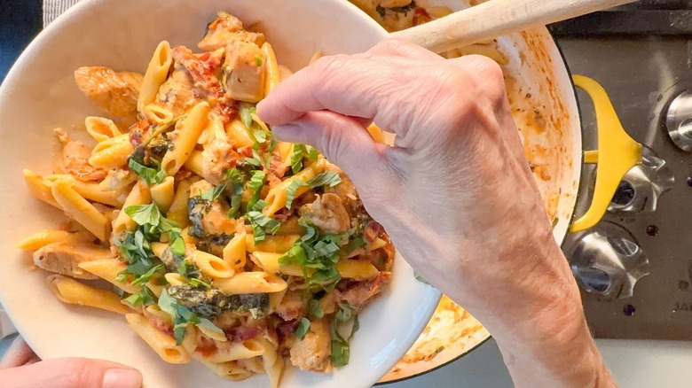 Garnishing high protein marry me chicken pasta with sliced basil leaves