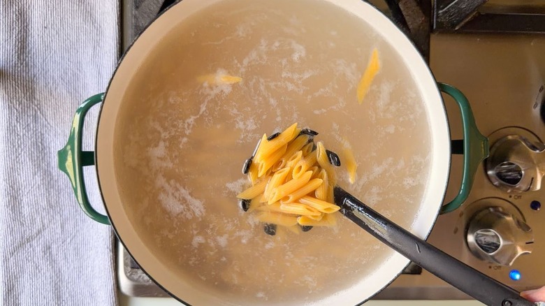 Cooking penne pasta in large pot on stove with pasta spoon