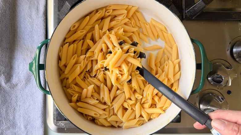 Tossing penne pasta with olive oil using pasta spoon in large pot on stovetop