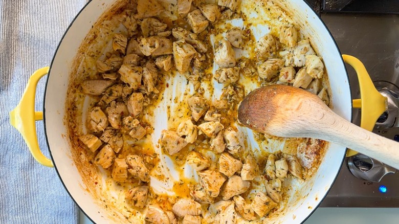 Stirring chicken and seasonings in large yellow pot with wooden spoon