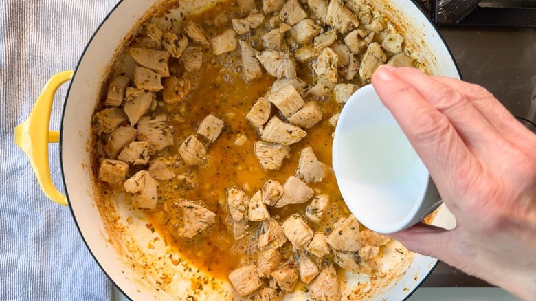 Adding white wine to chicken and seasonings in yellow pot on stovetop