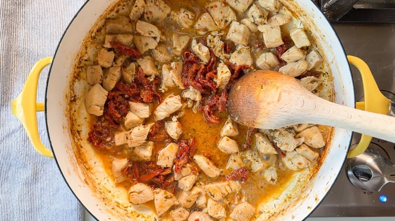 Stirring chicken, sun-dried tomatoes, and bone broth in yellow pot with wooden spoon