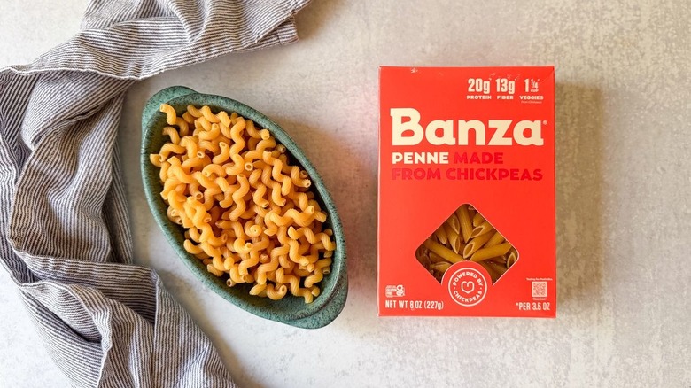 Box of Banza penne pasta and bowl of chickpea cavatappi pasta with towel