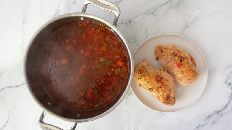 chicken breasts on a white plate next to a metal pot full of broth and vegetables