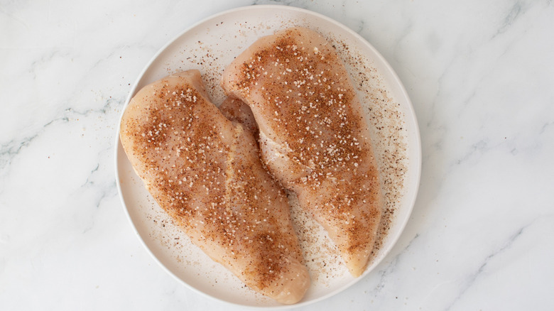 seasoned raw chicken breasts on a white plate