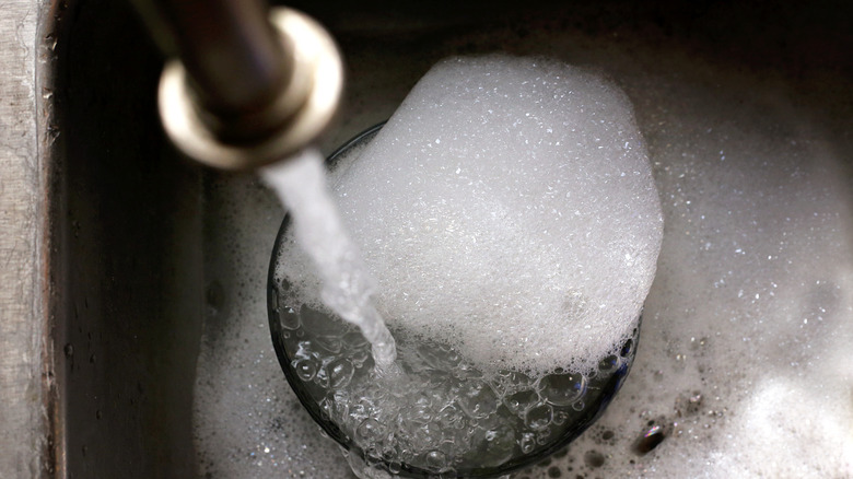 Water flowing out of the faucet over a soapy sink.
