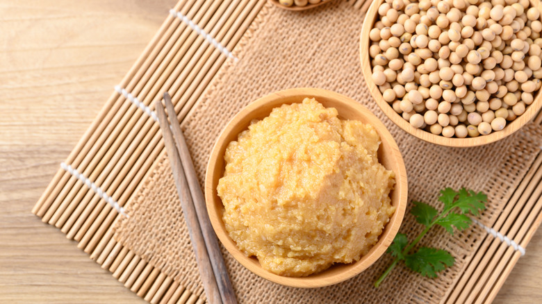 miso paste in a wooden bowl on a bamboo mat next to chopsticks and a bowl of soybeans