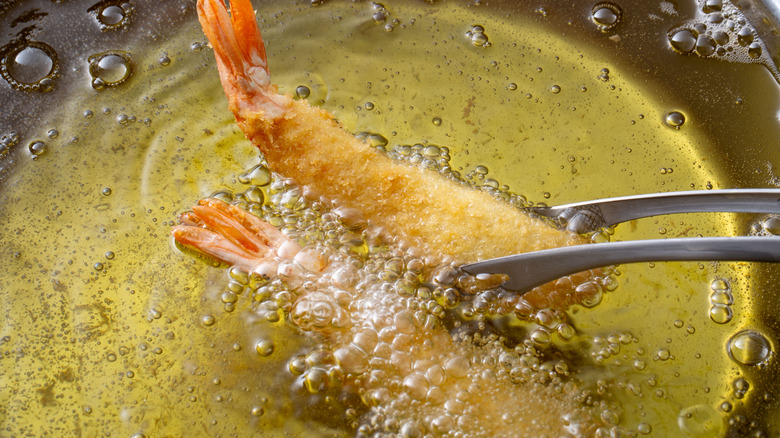 Deep frying tempura shrimp in oil with metal tongs