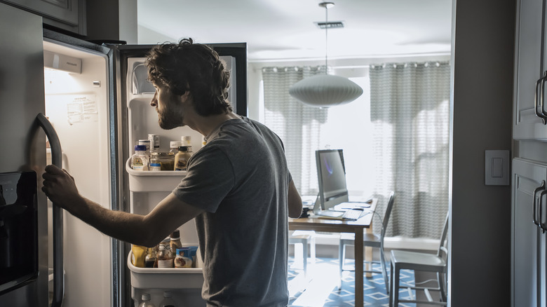A guy peering into the refrigerator in a dark room