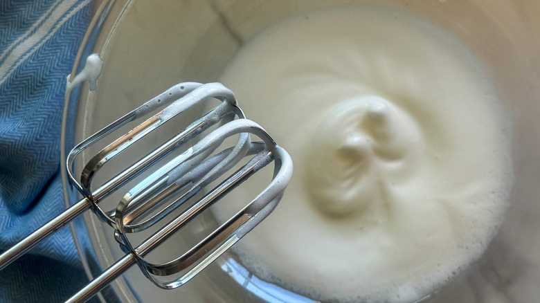 Hand mixer whisks in front of egg white mixture in bowl